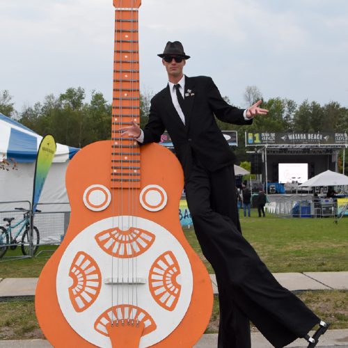 Stilt performer Incirque leaning up against a giant orange guitar